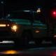 a tow truck with jkm towing logo illuminated by its lights, parked next to a car with an open hood in hamilton at night.